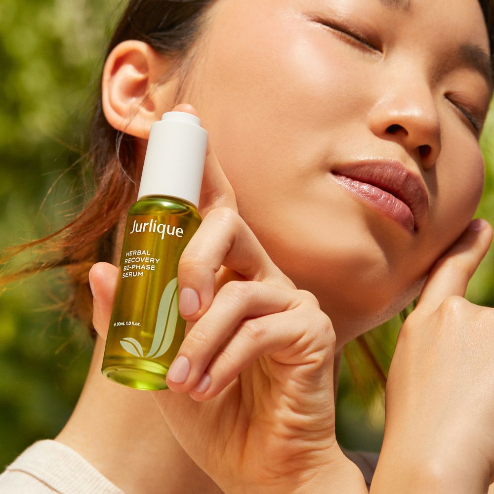 Woman holding a Jurlique skincare serum bottle with a blurred green background
